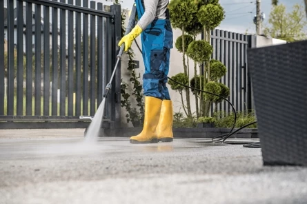 Persoon met gele laarzen gebruikt een hogedrukreiniger om een oprit schoon te maken.